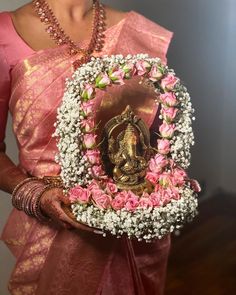 a woman in a pink sari holding a small mirror with flowers around it and a statue on top