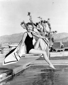 a woman in a bathing suit is sitting on a bench next to a pool and posing for the camera