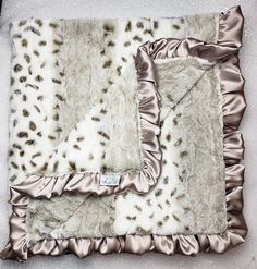 a blanket with silver and white fur on it sitting on top of a floor next to a pillow