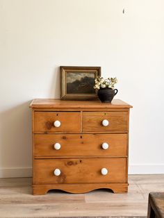 a wooden dresser with white knobs and a painting on top