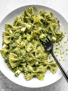 a white plate topped with pasta and broccoli covered in pesto sauce next to a fork