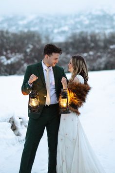 a bride and groom holding lanterns in the snow