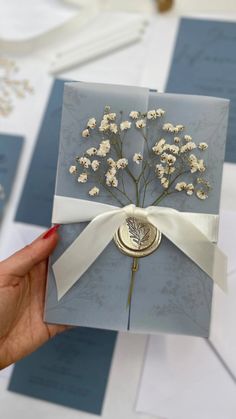 a hand holding a card with flowers on it and ribbon around the edge, in front of several other cards