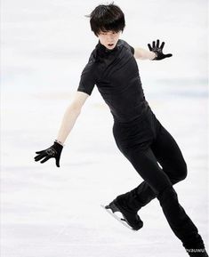 a man skating on an ice rink wearing black clothing and holding his arms out in the air