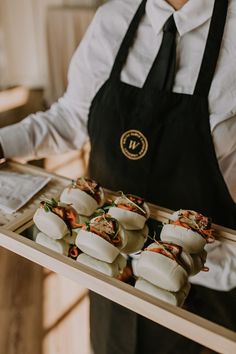 a person holding a tray with food on it and wearing an apron in front of them