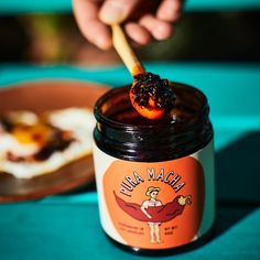 a person holding a spoon over a jar of jam