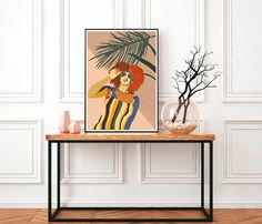 a table with a vase and plant on it in front of a wall mounted poster