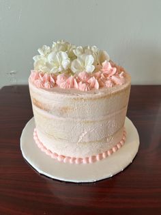 a white cake with pink frosting and flowers on top sitting on a wooden table