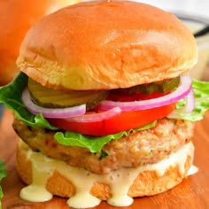 a chicken burger with lettuce, tomato and pickles on a wooden cutting board