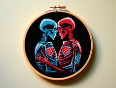 a cross stitched picture of two skeletons holding each other's hands in front of a white wall