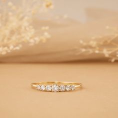 a yellow gold ring with five diamonds on it and a white flower in the background