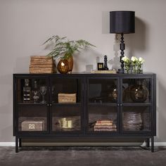 a sideboard with glass doors and plants on top in front of a gray wall