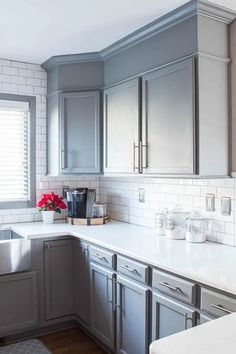 a kitchen with gray cabinets and white counter tops is pictured in this image, there are red flowers on the window sill