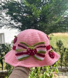 a pink crocheted hat with a bow on the brim is held up by someone's hand