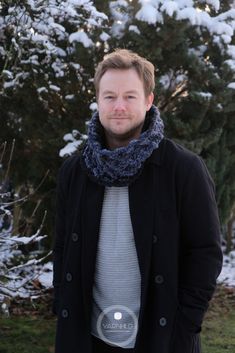 a man standing in front of snow covered trees with a blue scarf around his neck