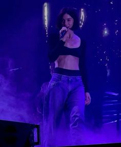 a woman standing on top of a stage with her hands in her pockets and holding a microphone