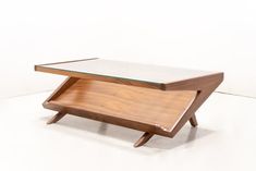 a table with a glass top and wooden legs on the bottom, in front of a white wall