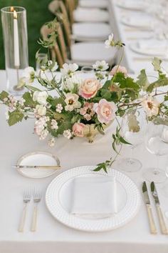 a table set with white plates, silverware and floral centerpieces on it