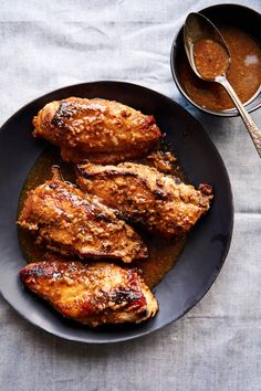 two pieces of chicken on a black plate with sauce in a bowl next to it