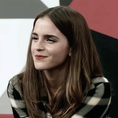 a woman with long hair sitting in front of a red and black wall smiling at the camera