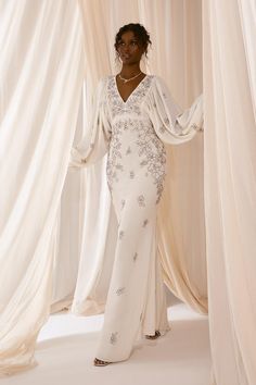 a woman standing in front of curtains wearing a white gown with beading on it