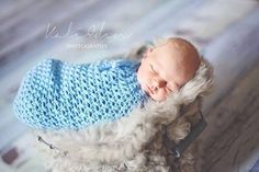 a newborn baby wrapped in a blue crochet blanket sleeping on top of a wooden floor