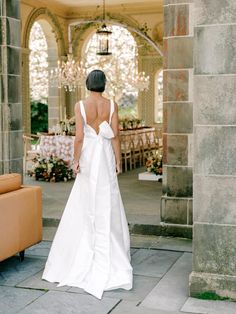 a woman in a white wedding dress walking into an outdoor area with tables and couches