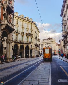 an orange trolley is going down the street in front of some old buildings and people