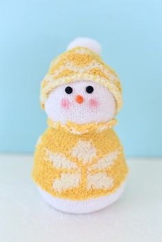 a small knitted snowman sitting on top of a white table next to a blue wall