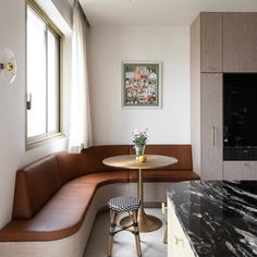 a corner table and bench in a room with marble counter tops, wood cabinets, and windows