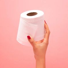 a woman's hand holding a roll of toilet paper in front of a pink background