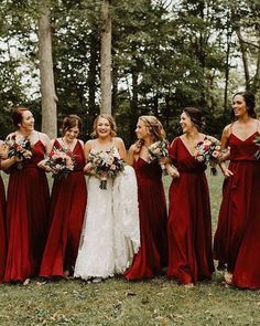 a group of women standing next to each other wearing red dresses and holding bouquets