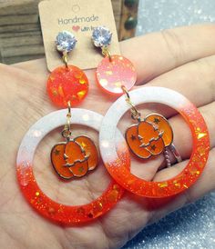 White and orange resin Halloween pumpkin earrings with holographic glitters and Jack O'Lantern charms The perfect pair of pendant earrings for Halloween night! They are entirely made in resin and glass pigments, cast in premium silicone molds. Each one of them is one of a kind since I mix resin with pigments for every single pair of earrings. Nickel-free studs with beautiful faceted crystal rhinestones and beautiful UV resin spooky Jack O'Lantern charms. Measures: approx. 7 cm (please see pictur Pumpkin Earrings, Holographic Glitter, Halloween Night, Uv Resin, Faceted Crystal, Pendant Earrings, Jack O Lantern, Crystal Rhinestone, Halloween Pumpkins