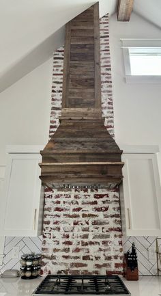 an old brick fireplace in a kitchen with white cabinets and a wooden mantle on the wall