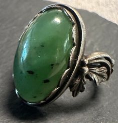 A vintage silver Genuine nephrite or Siberian Jade Decorative ring.  Size. 5 1/3, wt.- 5.5 grams, scalloped bezel set oval jade is approx. 11 x 17mm.  Lovely attention to details, hand textured silver with sculptural floral shoulders-very well made in very good condition. Heirloom Green Emerald Oval Cabochon Ring, Heirloom Green Oval Cabochon Emerald Ring, Art Deco Oval Cabochon Collectible Jewelry, Hallmarked Oval Green Jewelry, Antique Green Jewelry With Polished Finish, Antique Emerald Ring With Polished Finish, Formal Oval Jade Jewelry, Formal Green Oval Cabochon Jewelry, Oval Green Jewelry With Polished Finish