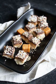 there are many pieces of dessert on the black plate and one is cut into cubes