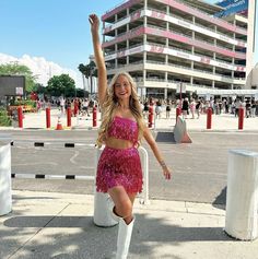 a woman in a pink dress and white boots posing for the camera with her arms up