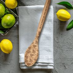 a wooden spoon sitting on top of a white towel next to lemons and green leaves