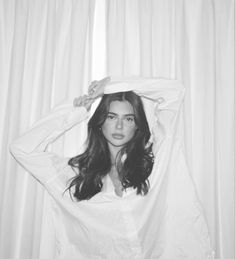 a woman with long hair is standing in front of curtains and holding her hands on her head