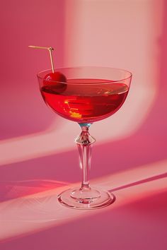 a red drink in a wine glass with a stick sticking out of the top, on a pink background