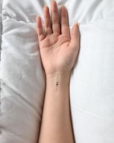 a person's hand with a tiny tattoo on their left wrist, resting on a white pillow