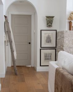 a living room with white walls and wood flooring next to a ladder leading up to the door