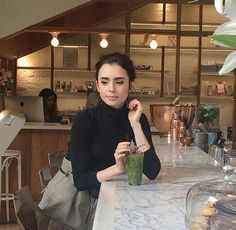 a woman sitting at a bar with a green smoothie in front of her,