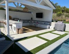 an outdoor living area next to a swimming pool and covered patio with grass on the ground