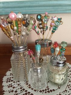 some glass jars are sitting on a doily with beads and other items in them