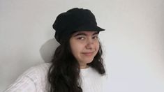 a woman with long hair wearing a black hat and white shirt, standing in front of a wall