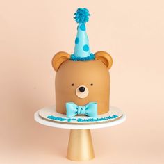 a birthday cake with a teddy bear wearing a party hat and bow tie on top