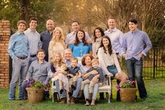 a large family poses for a photo in front of a brick wall and fence with potted plants