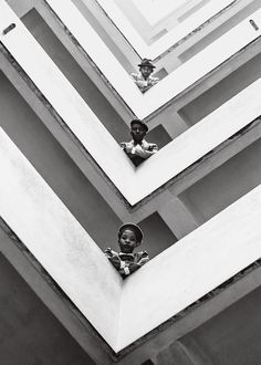 black and white photograph of two children looking out from the windows of an apartment building