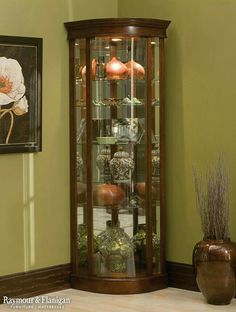 the corner of a room with a glass case and vases on the floor next to it